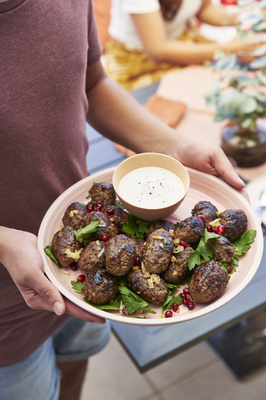 A shared plate of grilled lamb koftas passed around an outdoor table